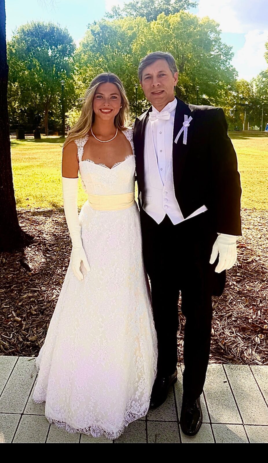Woman in a white gown and long white gloves beside a man in formal attire and white gloves.